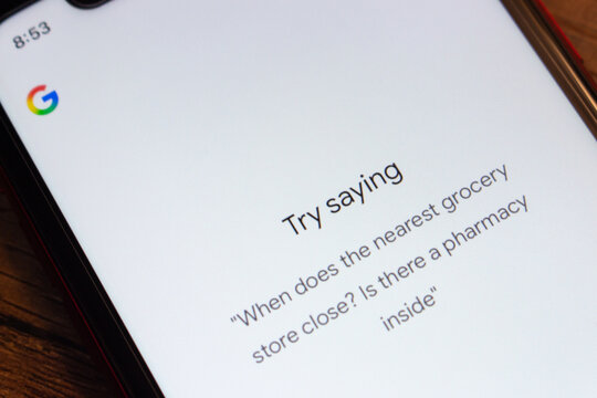 Mexico City, MEXICO - Mar 31 2026 : Close-up of a smartphone showing the Google Assistant voice prompt screen with "Try saying" and an example query about a grocery store and pharmacy.