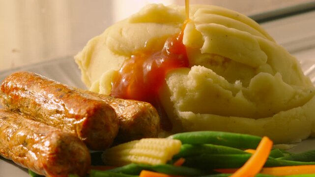 Bangers and Mash Potato with Vegetables and Gravy Pouring in Slow Motion in Natural Light. British Cuisine Dinner Food. 4K.