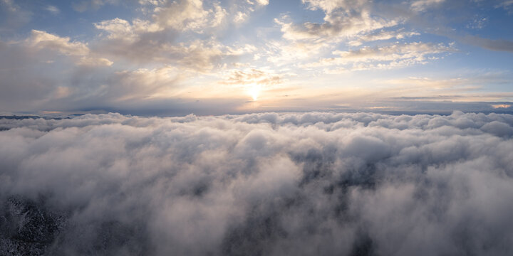 Aerial view of a thick blanket of white clouds under a golden sunset sky with soft light breaking through the horizon.