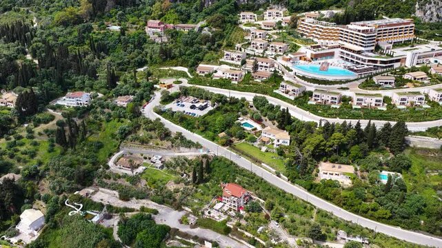 Aerial Drone View of Angsana Corfu Resort and Spa in Greece, Luxury Mediterranean Hotel Featuring Stunning Infinity Pools, Lush Green Hills, Coastal Roads, and Turquoise Sea in Benitses, Corfu.