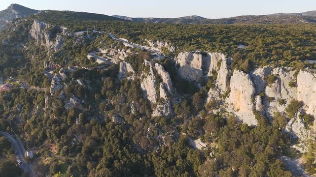 Drone view of steep limestone cliffs and dense forest terrain near Baunei under soft evening light, drone
