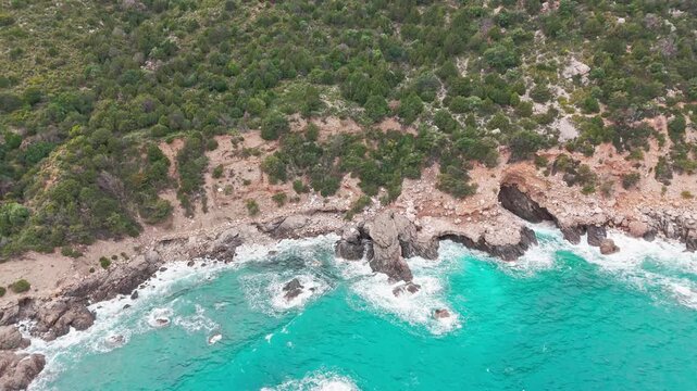 Rocky shoreline with turquoise water and dense greenery near Baunei Sardinia coastline, drone
