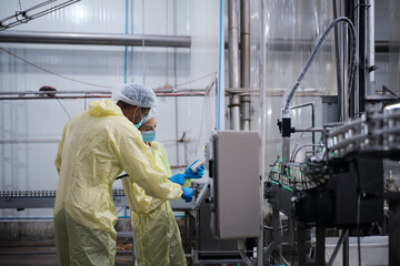 Fototapeta premium Two industrial engineer supervisors examine quality of steel containers on factory conveyor belt, inspect production process in canned food manufacture, and protective uniforms for hygiene operations.