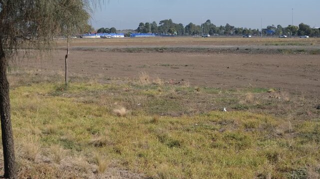 Vast undeveloped land and cleared earth in Manor Lakes, Melbourne, Australia; a vacant greenfield site prepared for residential development with a distant view of urban infrastructure and traffic.
