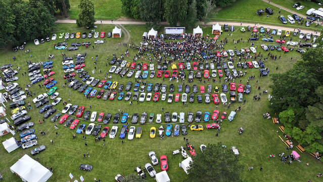 La Chapelle-de-Guinchay, France - 01 June 2024: Aerial view of a large gathering of colorful sports cars parked in rows on a green field during a car meet with a crowd of people.