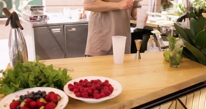 Cocktail making. Tropical drink. Unrecognizable professional barman hands pouring alcohol using tool strainer for fruit fresh syrup in cafeteria.