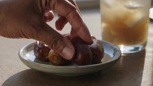 Hand placing a sweet dried date on a plate with a drink nearby