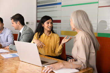 South Asian businesswoman engaging in conversation with woman colleague during group meeting in...