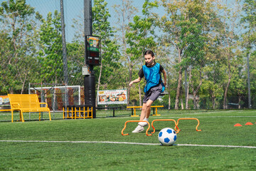 Obraz premium World cup concept with soccer ball or football player, youth soccer player practices hurdle drill on outdoor field in sunny park