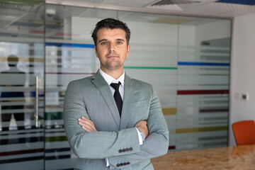 Obraz premium Adult Caucasian businessman posing for office portrait standing with arms crossed in boardroom, represent corporate success, professionalism in business. Entrepreneurship, executive management concept