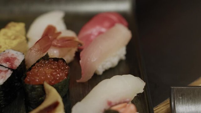 Hand using chopsticks to grab fatty tuna nigiri from assorted sushi platter with ikura and shrimp
