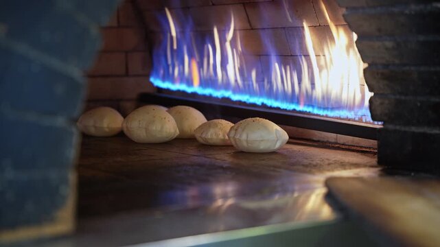 fresh pita bread puffing up inside a traditional brick oven with vibrant blue gas flames. Authentic culinary footage perfect for food documentaries and restaurant advertisements.