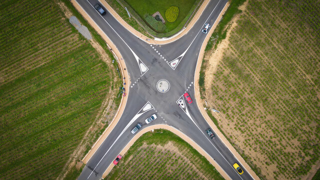 Aerial view of a rural road intersection with cars driving through green vineyards and agricultural fields La Chapelle-de-Guinchay, Bourgogne-Franche-Comte, France.