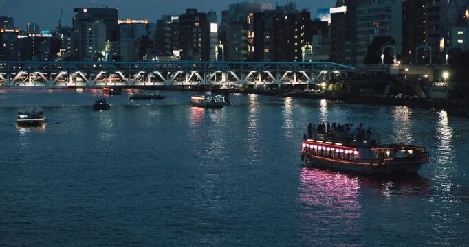 Japanese traditional yakatabune cruise boat with tourists sailing on Sumida river at evening. Tokyo city skyline, illuminated bridges, buildings in urban scenic view. Cityscape static panorama