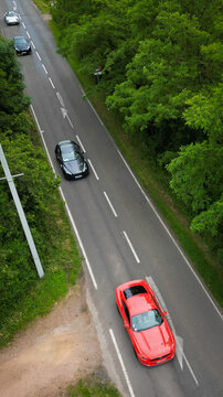 Aerial view of a red sports car and other vehicles driving along a paved road surrounded by dense green trees La Chapelle-de-Guinchay, Bourgogne-Franche-Comte, France.