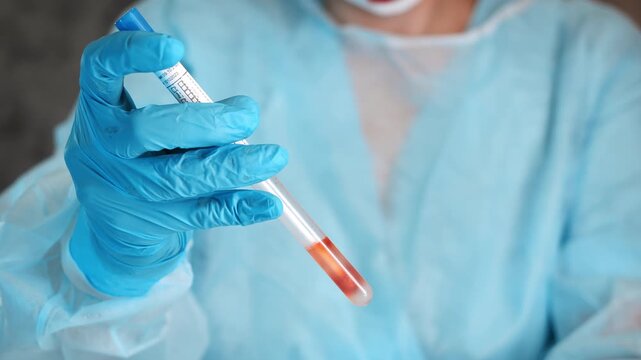 Close up of laboratory worker in protective suit holding medical sample tube during scientific testing and clinical diagnostics in laboratory.