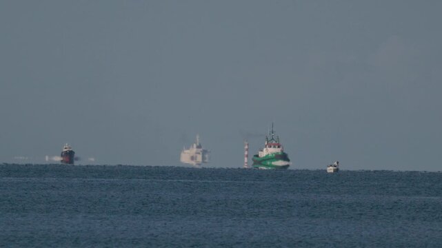 Ships travel across the sea near a lighthouse in the distance during the day in clear weather