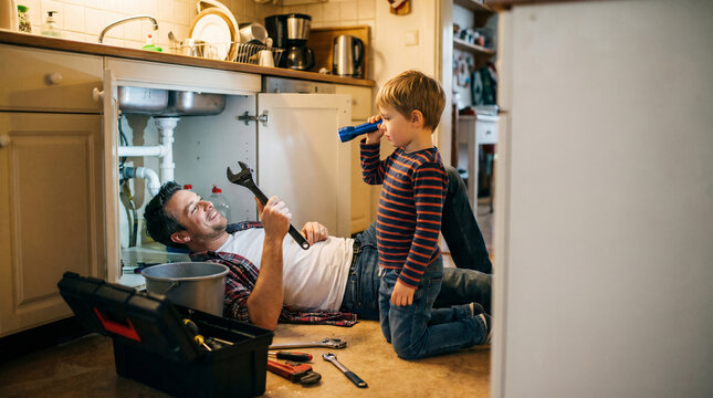 Celebrating Father's Day with quality time, a caring dad shows his eager son how to fix household plumbing, building cherished memories and practical knowledge