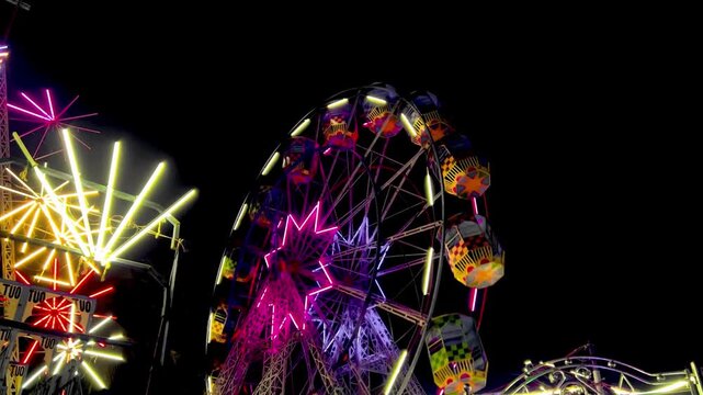 Brightly lit ferris wheel spins at amusement park at night with colorful lights and star shapes creating festive atmosphere for fairground fun and entertainment.