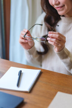 Vertical closeup image of a woman holding glasses while writing on notebook at home