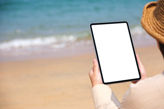 Mockup image of a woman holding a digital tablet with blank desktop screen by the sea