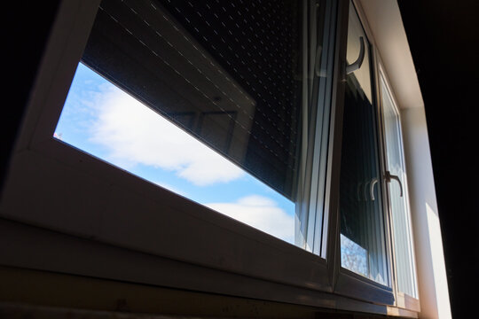 Open window with partially lowered roller shutter and blue sky