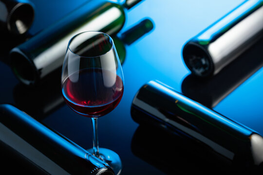 Glass and bottles of red wine on a black reflective background.