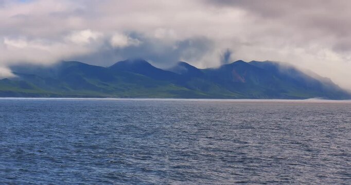 Wide coastal seascape with calm ocean water dark mountain island and low clouds Moody landscape with blue tones distant shoreline overcast sky and atmospheric travel dramatic weather background