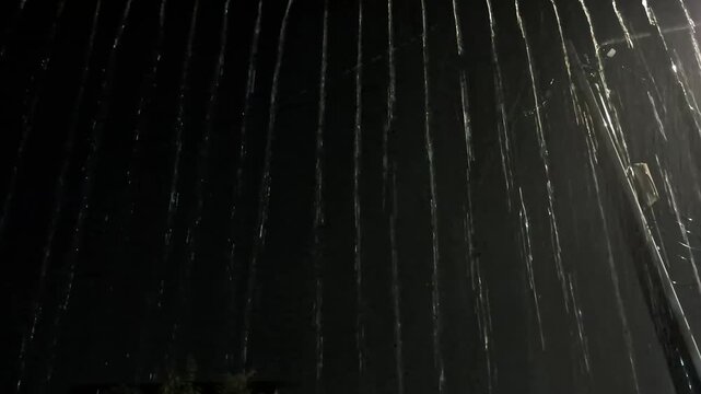 Close-up of heavy rain streaks falling from the roof, creating a water curtain effect against a stark black night background.
