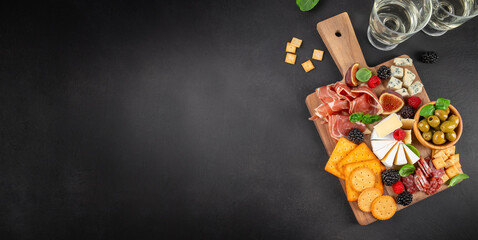 Charcuterie board with cheese prosciutto olives and wine on black background with copy space