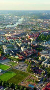 Vertical video. Gothenburg, Sweden. Ullevi stadium and the Gota Alv river, aerial panoramic view over terracotta rooftops, green parkland, and the historic city center at sunset. Drone footage, Depar