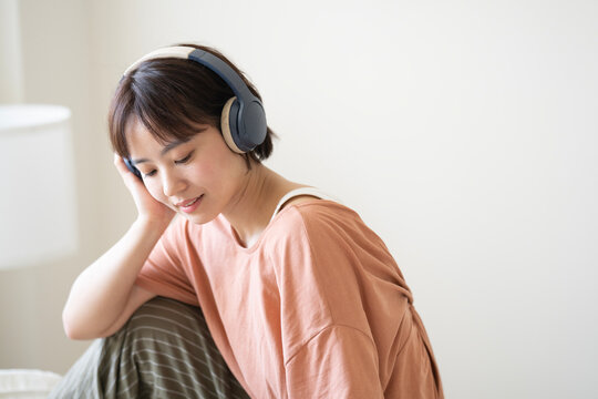部屋でヘッドフォンをして音楽を聴いている女性