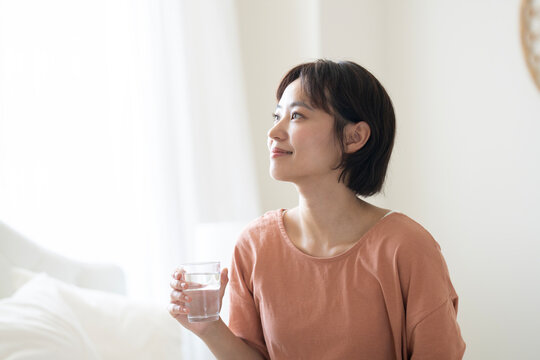 グラスに入った水を持って外を見ているショートカットの女性