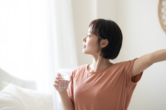 グラスに入った水を持って外を見ているショートカットの女性