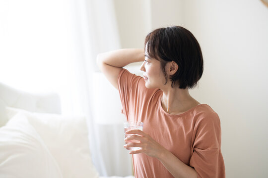 グラスに入った水を持って外を見ているショートカットの女性