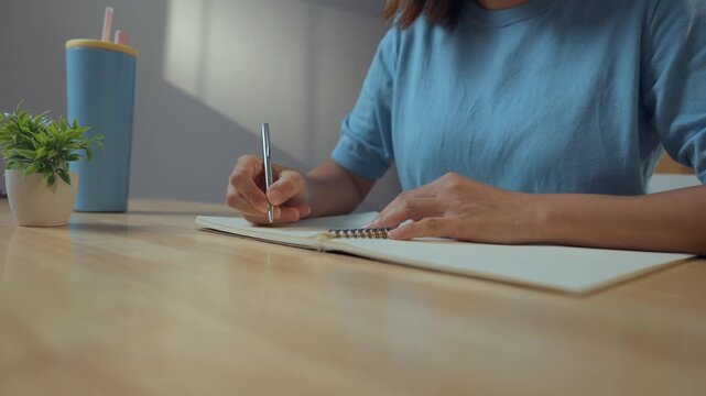 Close-up image of a woman's hand holding a pen and writing on a surface, possibly a notebook or a desk.
