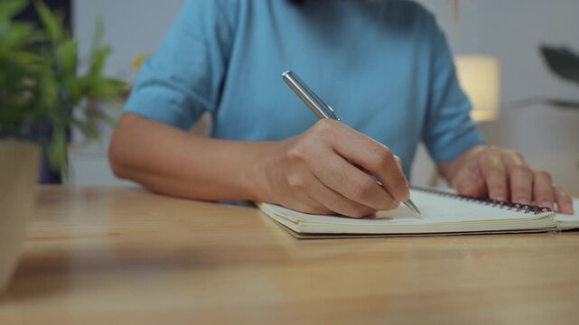Close-up image of a woman's hand holding a pen and writing on a surface, possibly a notebook or a desk.