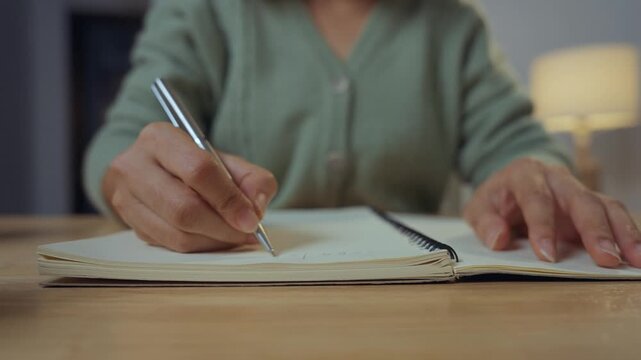 Close-up image of a woman's hand holding a pen and writing on a surface, possibly a notebook or a desk.