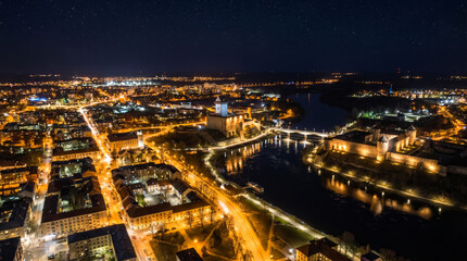 Naklejka premium Aerial view of a city at night with illuminated buildings and a river reflecting the lights.