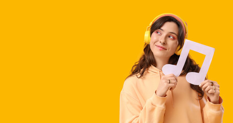 Naklejka premium Young woman with paper music note and headphones on yellow background