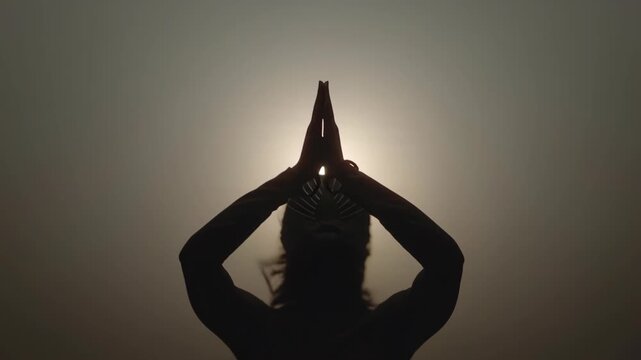Person practicing silhouette prayer pose against golden sunrise sky