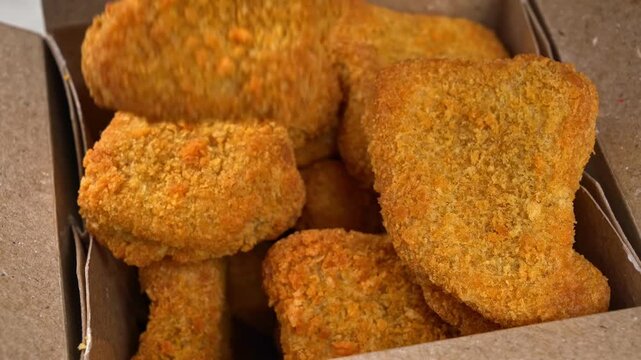 Hand grabbing crispy chicken nugget from fast food takeout box