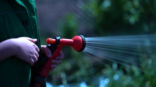 Person watering plants with a garden spray nozzle outdoors