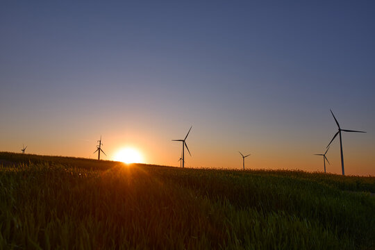 Wind turbines at sunset in green field &ndash; renewable energy, clean power, sustainable future.