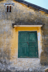 Fototapeta premium Weathered yellow wall and green window in Hoi An Vietnam
