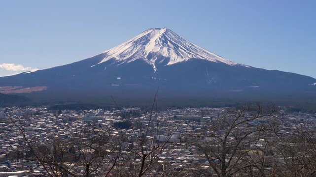 Slow motion landscape pan of Mount Fuji snowy peak surrounded by national park forest woodlands and Fujiyoshida suburban housing in a valley viewed from Arakurayama Sengen Park in Japan tourism nature