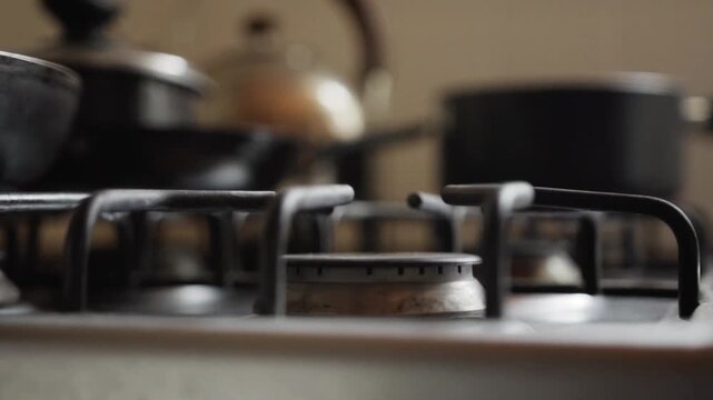 Closeup view of gas stove burner igniting with blue flame inside home kitchen surrounded by cookware and domestic interior setting