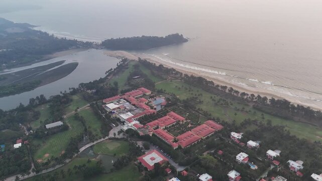 Wide cinematic aerial of Golf Ground and Spa Resort Goa showcasing structured resort blocks, coastal greenery, calm backwaters, and an uninterrupted shoreline stretching into the horizon.