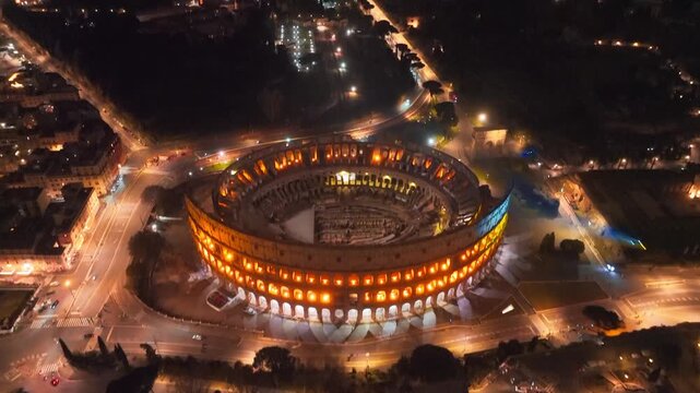 Aerial drone Colosseum night view in Rome and the city lights of Roma. The iconic Roman monument is lit up in blue and yellow to show solidarity with Ukraine, February 24