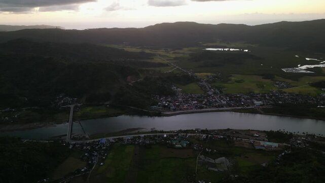 Scenic aerial flyover of Bato River in Catanduanes, Philippines with rural barangay village, bridge, and surrounding mountain landscape